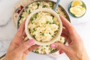 Hands holding bowl of risotto rice.