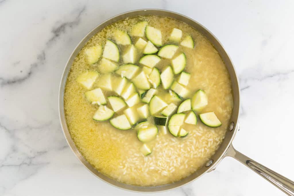 Broth with risotto and zucchini in frying pan.