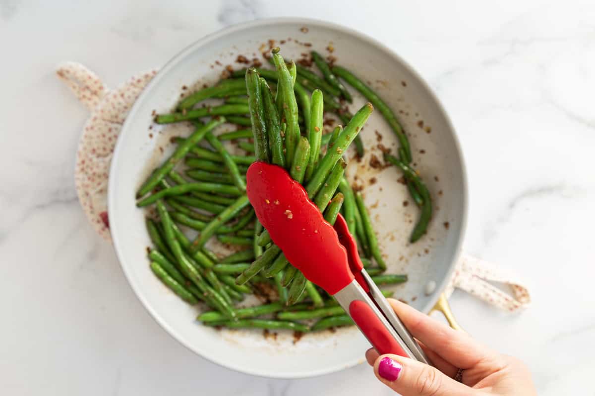 Green beans with thongs in frying pan for sesame green beans.