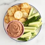 Beet hummus with cucumber sticks and crackers on plate.