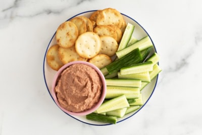 Beet hummus with cucumber sticks and crackers on plate.