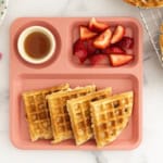 Whole wheat waffles on kids pink plate with sides.