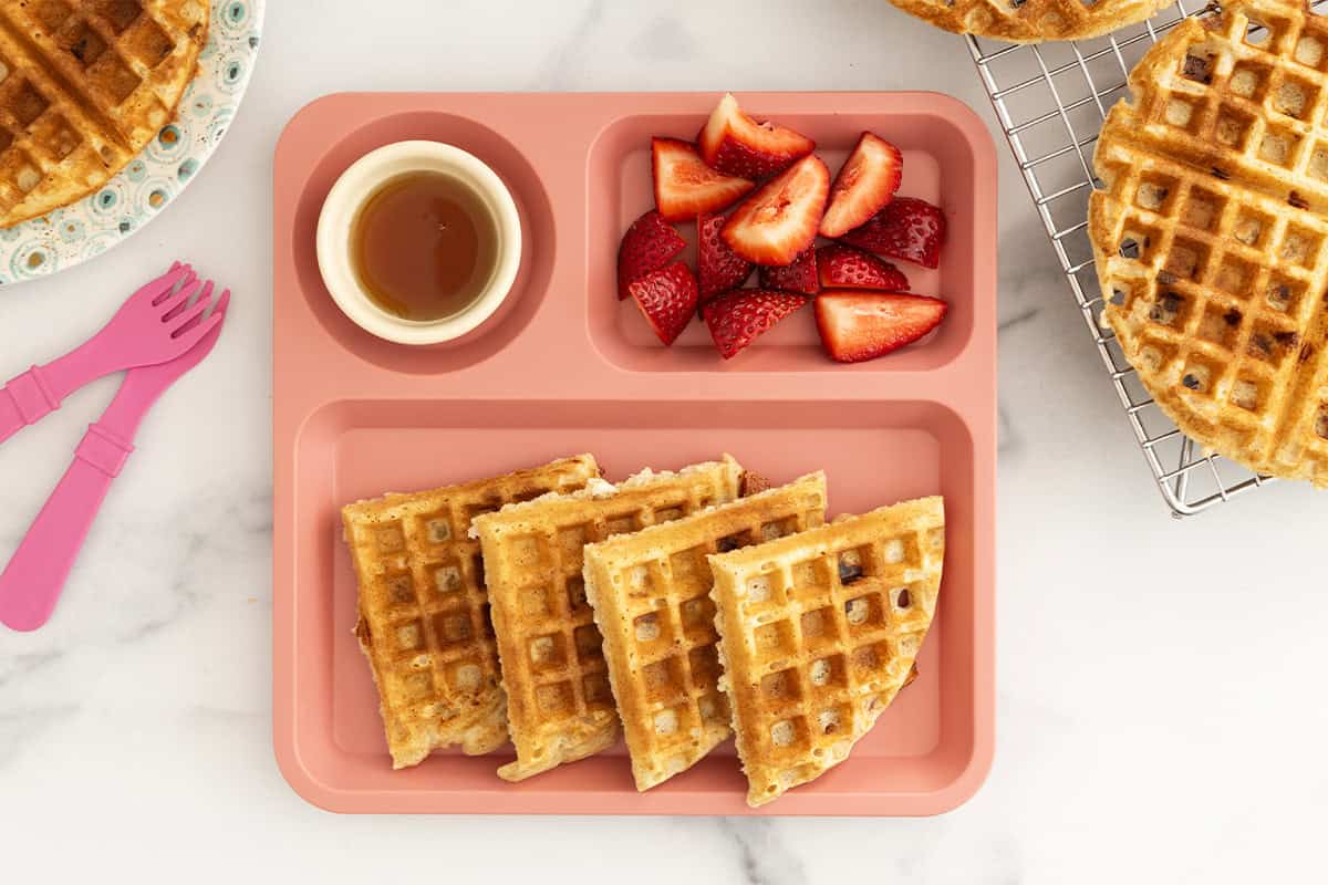 Whole wheat waffles on kids pink plate with sides. 