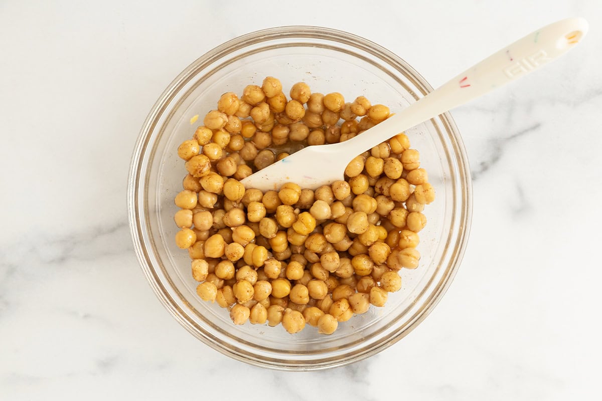 Chickpeas in glass bowl with spatula stirring them.