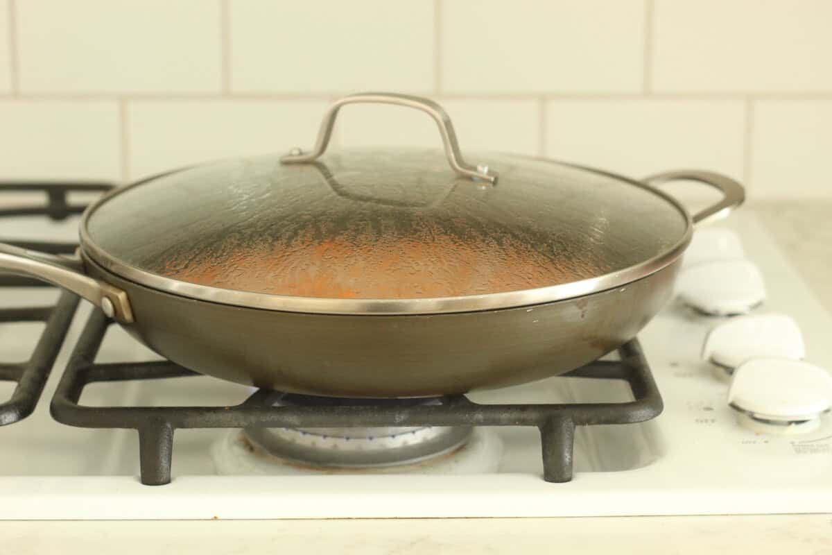 Frying pan with lid cooking baby carrots.