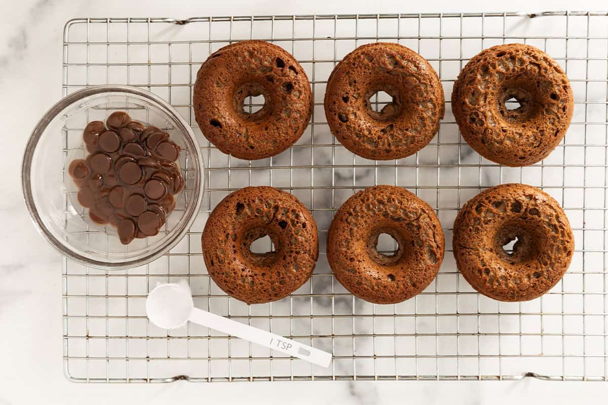 Chocolate baked donuts on cooling rack with melted chocolate on side.