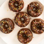 Chocolate baked donuts with frosting and sprinkles on white plate.