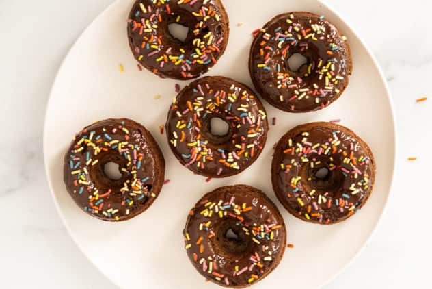 Chocolate baked donuts with frosting and sprinkles on white plate.