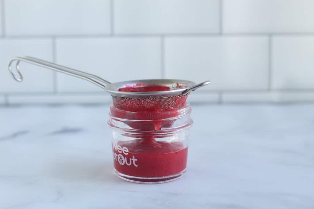 Raspberry puree being strained into a glass jar.