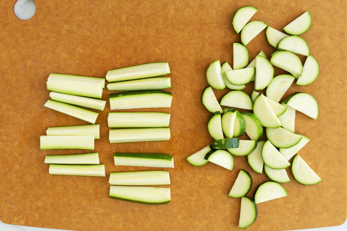 Zucchini cut into half moons and sticks on cutting board.