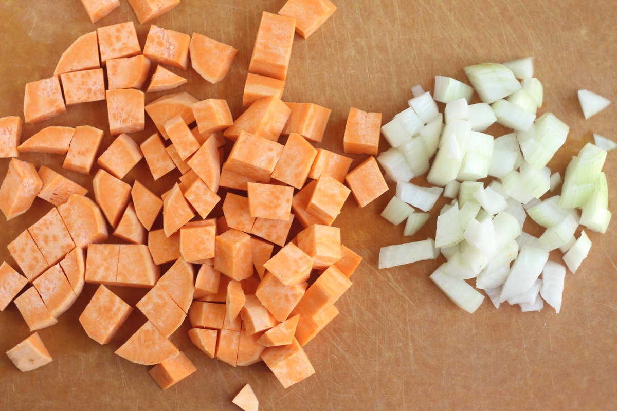 Sweet potato and onion diced on cutting board. 