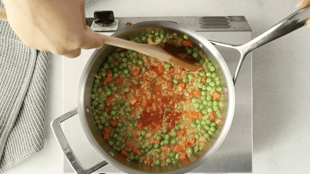 Spoon stirring veggies in pot for alphabet soup.