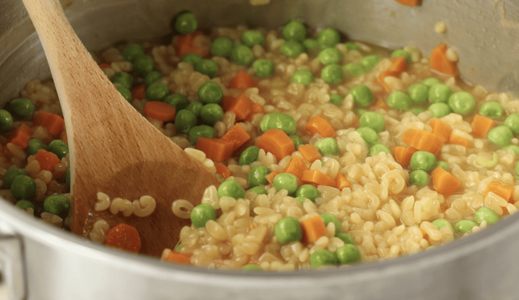 Alphabet soup in pot being stirred with wooden spoon.