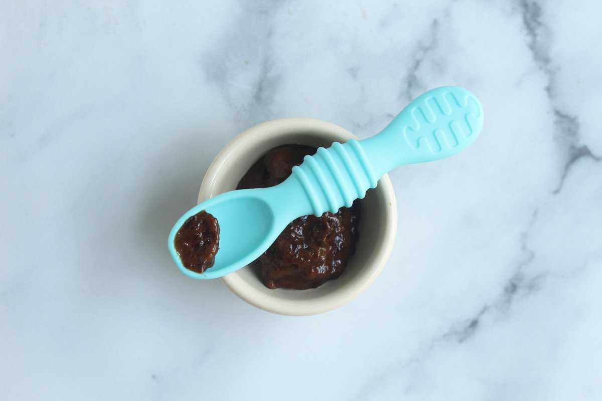 Prunes for baby on a blue spoon over bowl