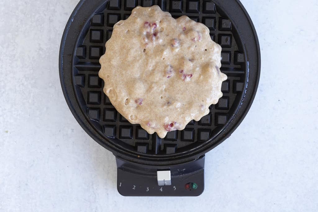 Waffle with raspberries in waffle iron before cooking.