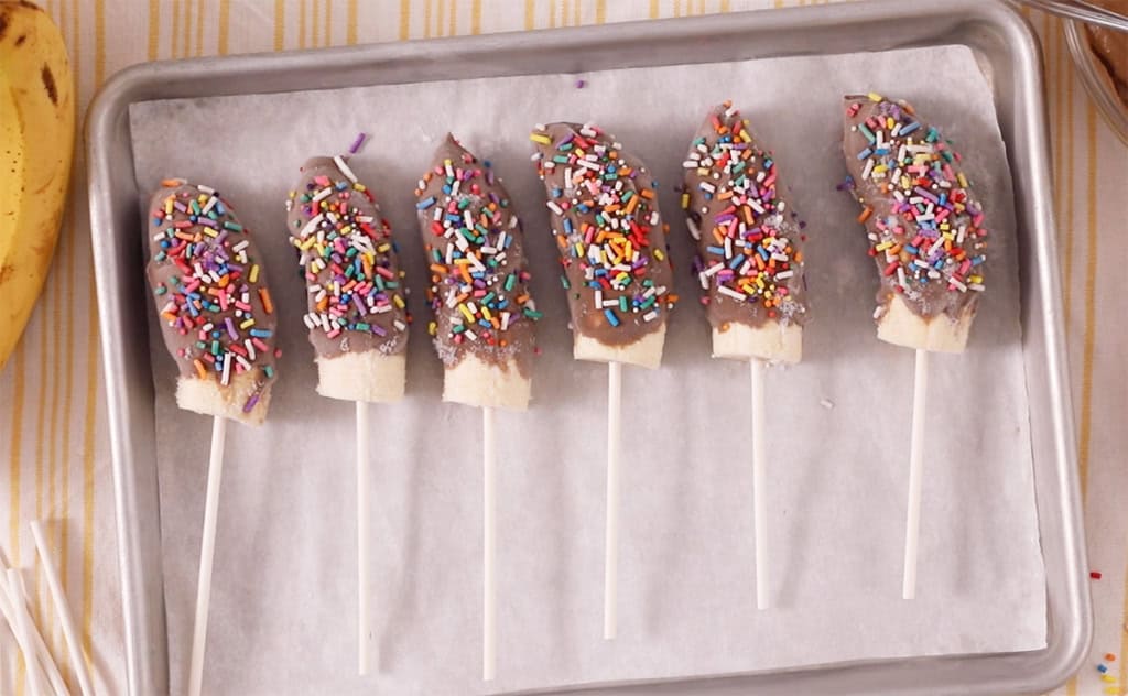 Chocolate covered bananas on baking sheet.