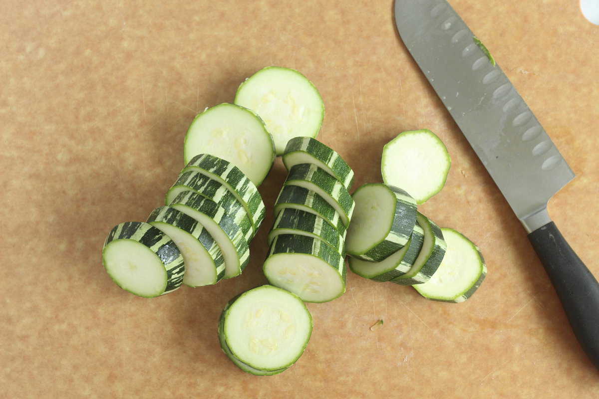Zucchini cut into slices on cutting board.