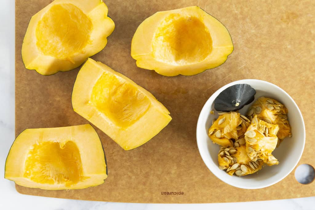 Acorn squash with seeds scooped out on cutting board.