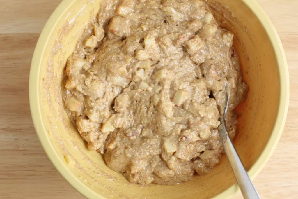 Batter for Apple Cake in yellow bowl with spoon.