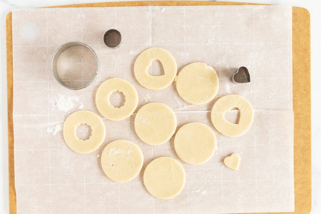 cutting out rounds of jam sandwich cookie dough with cookie cutter.