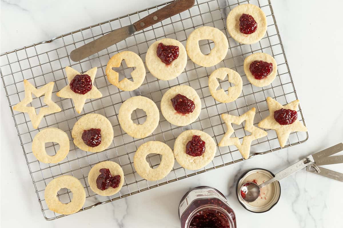 assembling jam cookies on wire rack with raspberry jam jar.