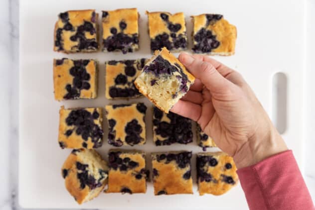 Blueberry yogurt cake cut into pieces with hand holding one.