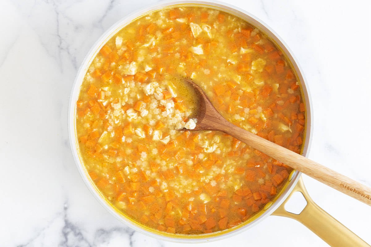 Chicken and stars soup in pot with wooden spoon.