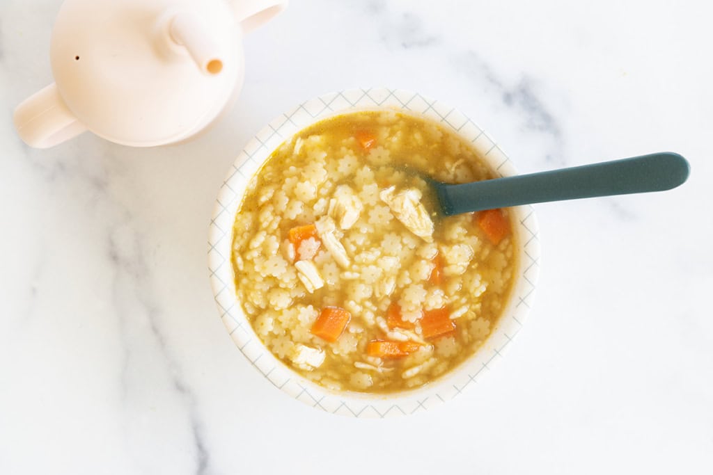 Chicken and stars soup in bowl with spoon.