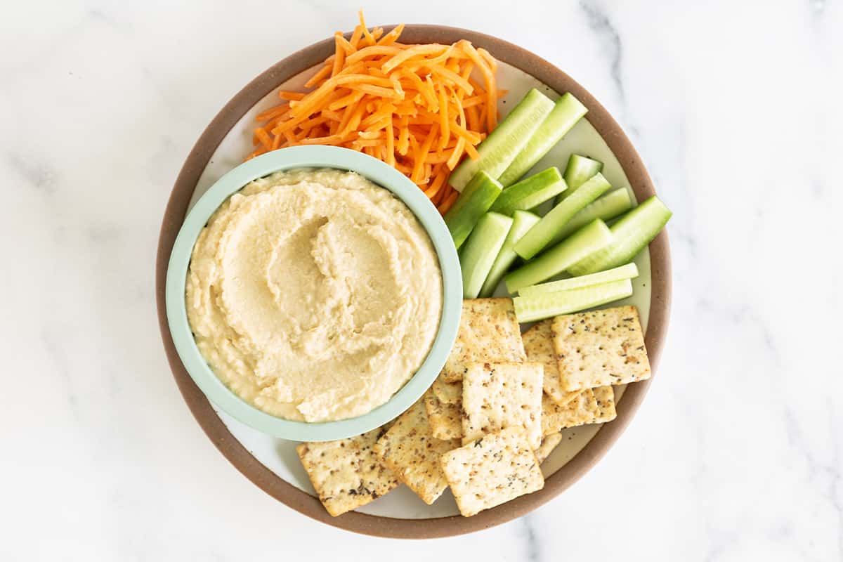 creamy hummus in bowl on plate with veggies