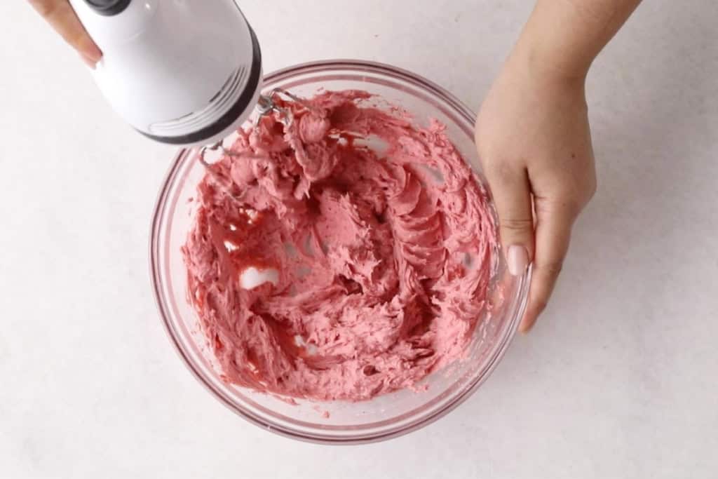 Strawberry cream cheese frosting being whipped with hand held mixer.