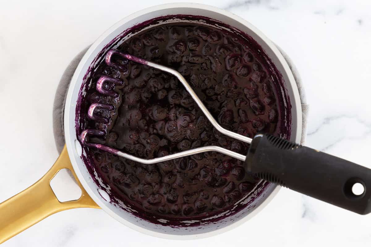 Potato masher in pan with blueberry sauce. 