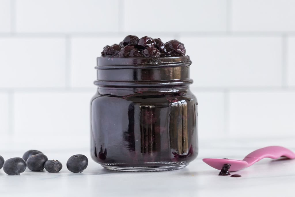 Blueberry sauce in mason jar with pink spoon on side.