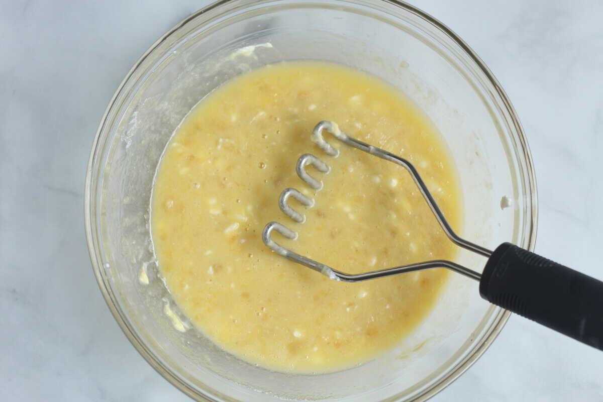 Banana mashed in a glass bowl with potato masher. 