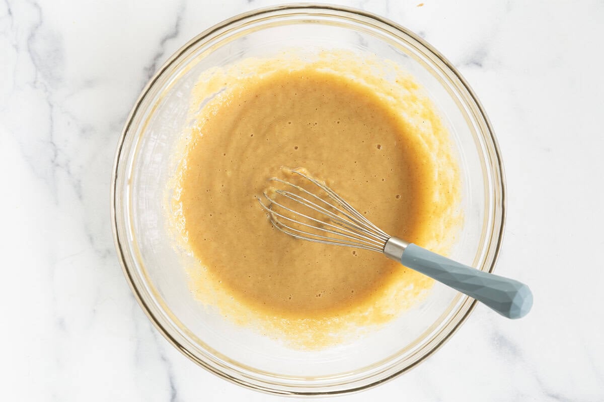 Wet ingredients for applesauce bread in glass bowl with whisk. 