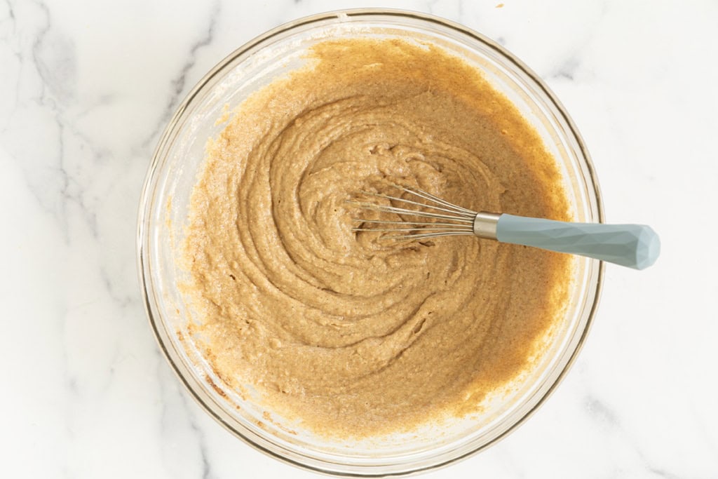 Batter for applesauce bread in glass bowl with whisk.