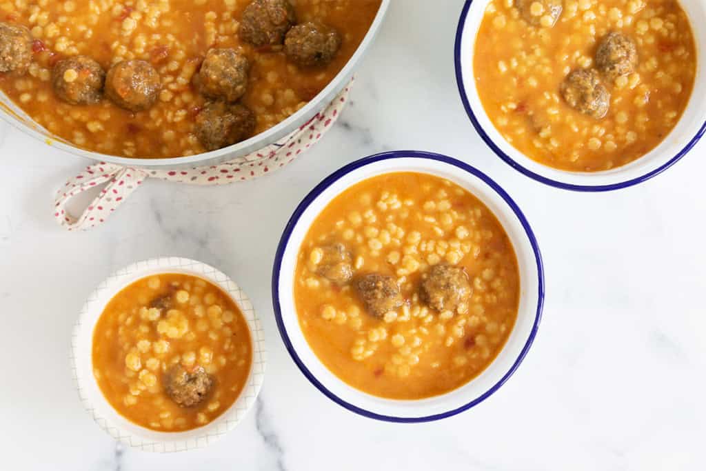 Meatball soup in pan and three bowls.