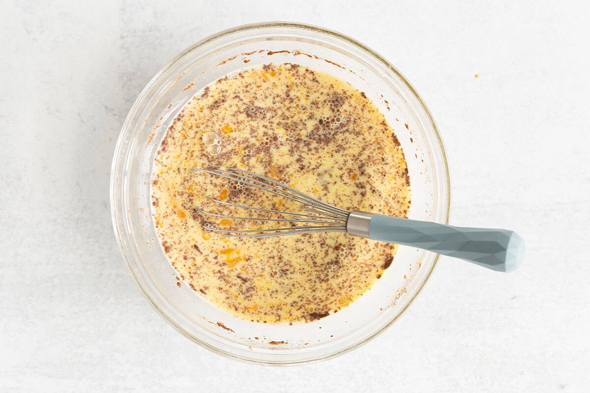 Batter for french toast casserole in glass bowl with whisk. 