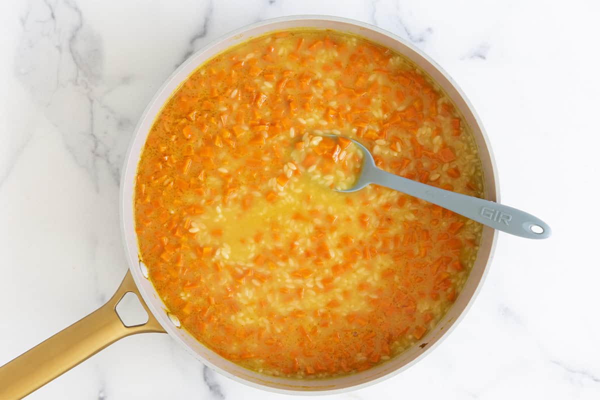 Carrots, broth and orzo in pan for orzo soup.