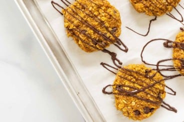 Pumpkin oatmeal cookies on baking sheet with chocolate drizzle.