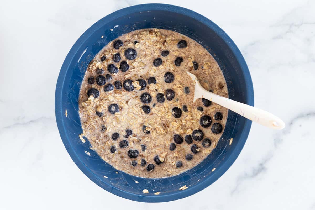 Blueberry baked oatmeal batter in blue bowl with spoon.