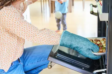 Mom getting food out of oven with child in background.