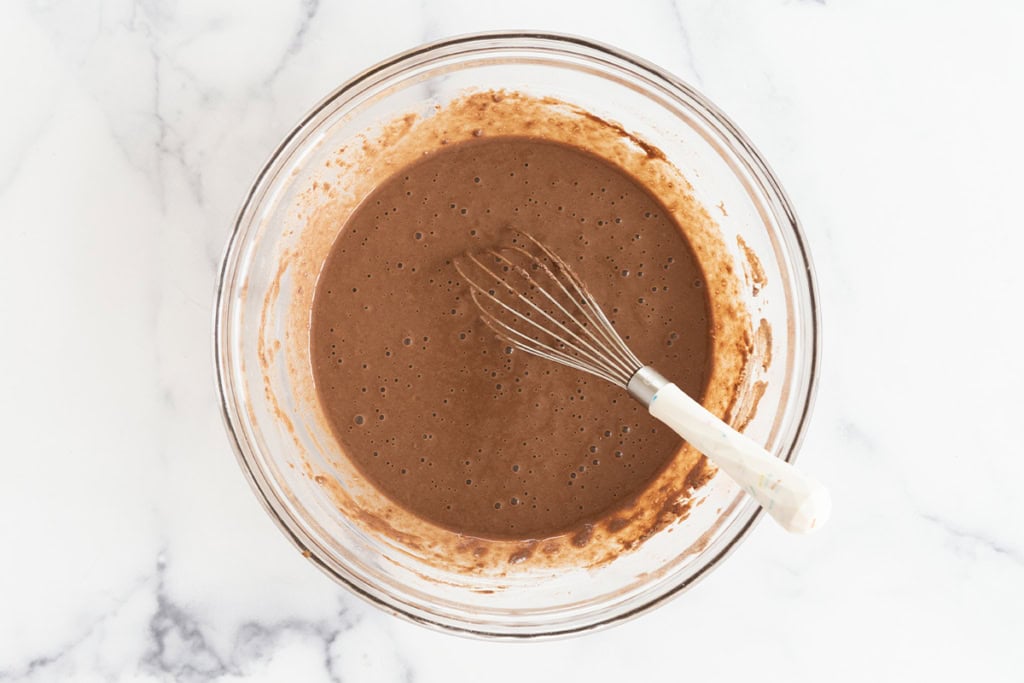 Batter for chocolate pancakes in glass bowl with whisk.