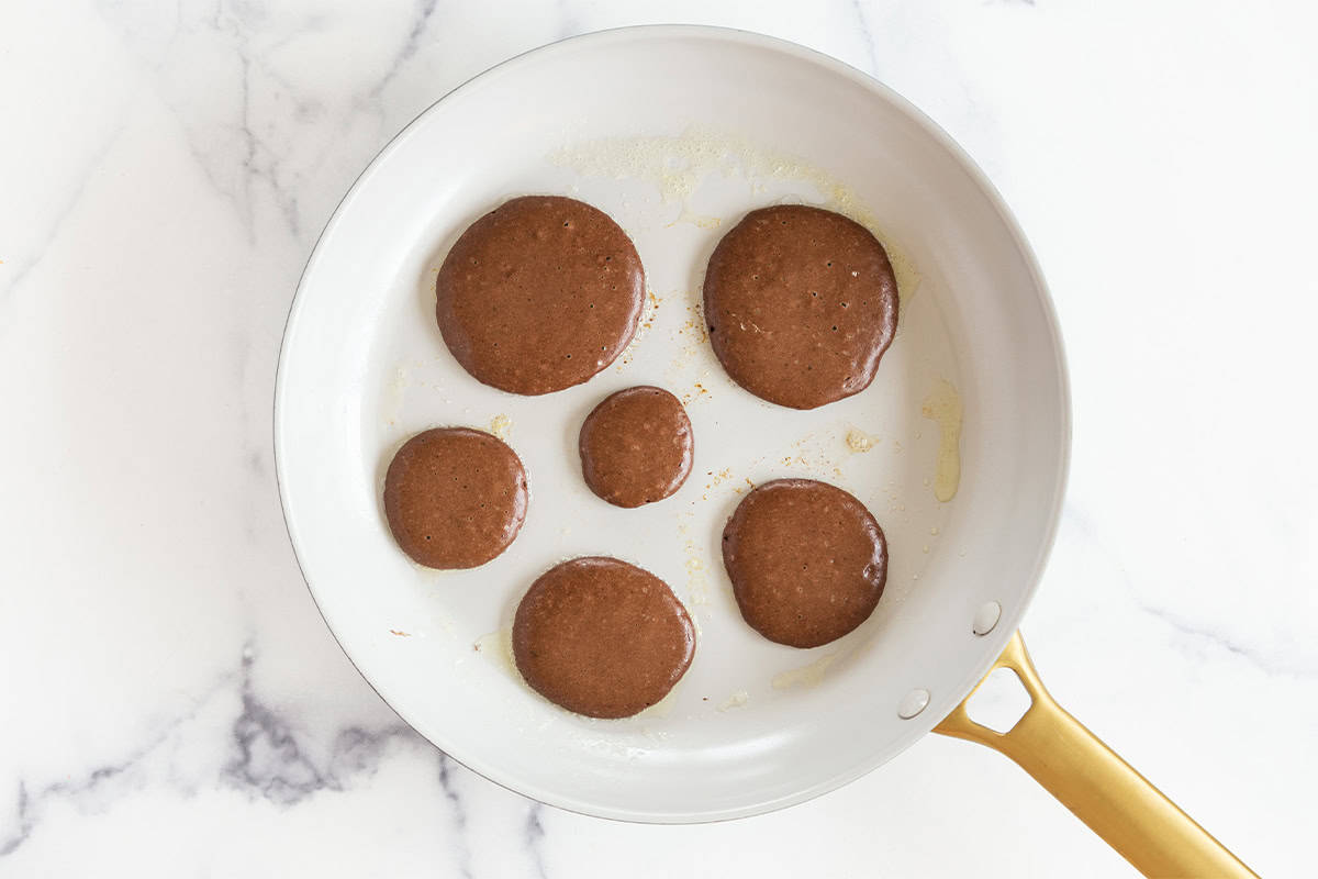 Chocolate pancakes in pan before flipping.