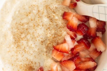 Baby oatmeal in bowl with strawberries and spoon.