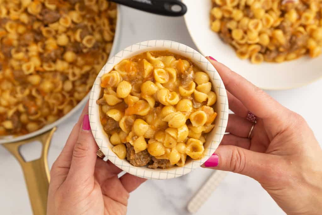 Hands holding bowl of cheeseburger pasta.