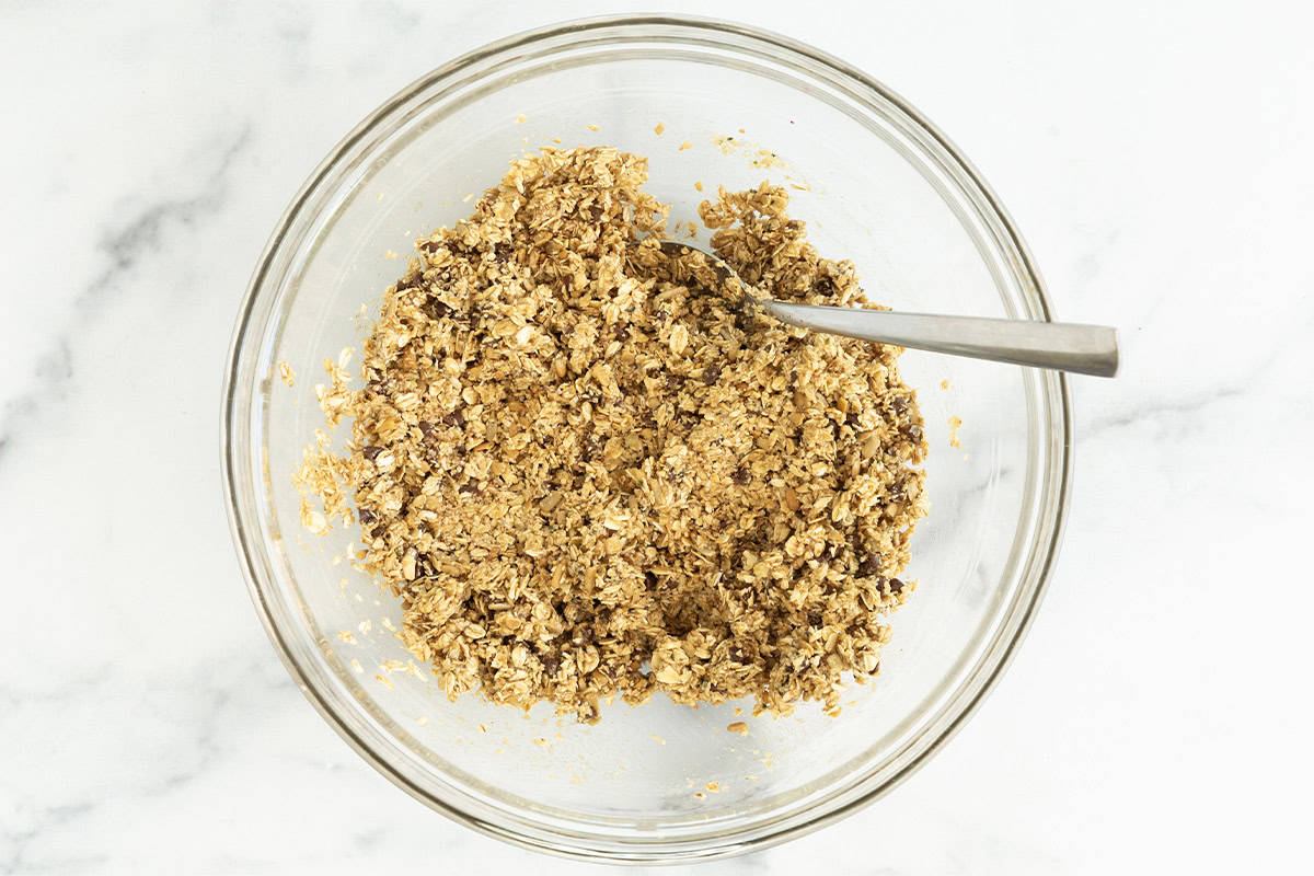 Mixture for chewy granola bars in glass bowl with spoon.