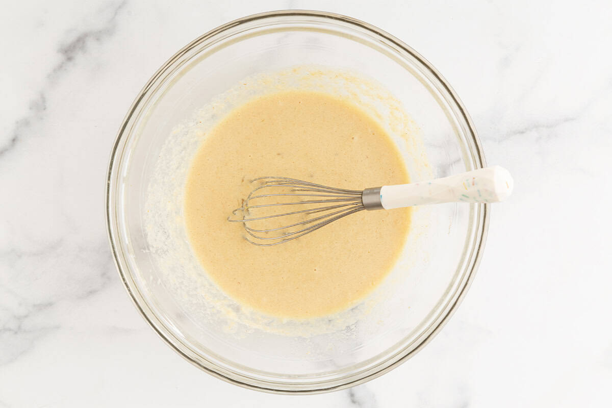 Wet ingredients for oatmeal muffins in glass bowl with whisk.