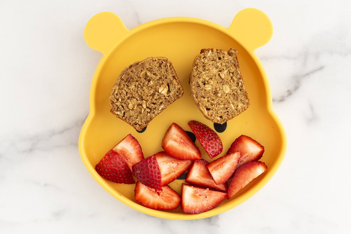 Oatmeal muffin on kids plate with strawberries.