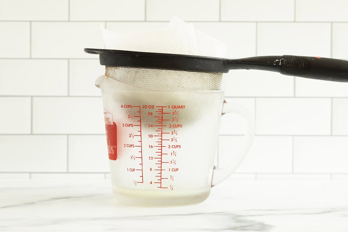 greek yogurt in strainer over measuring cup.