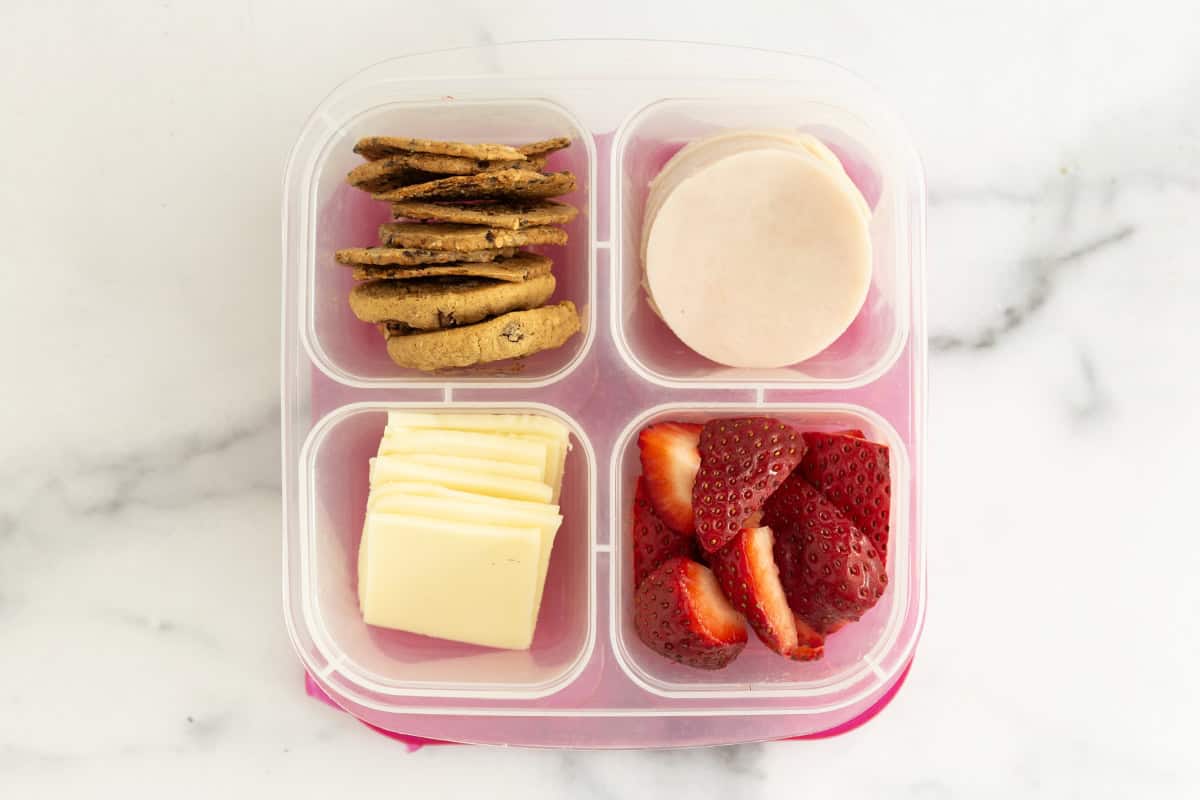 Homemade lunchable with cheese, cookies, strawberries and ham.